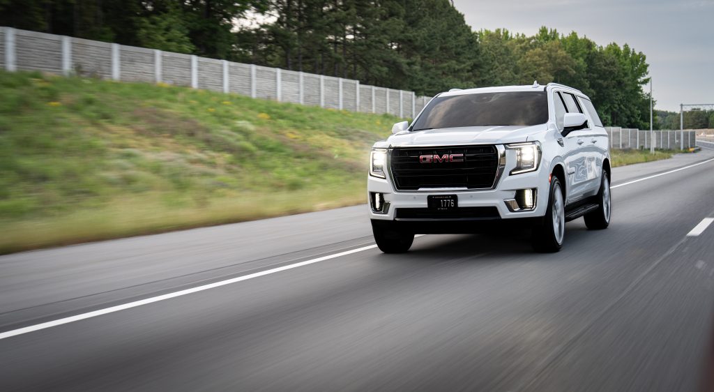 White GMC SUV speeding along a highway with blurred roadside greenery in the background.