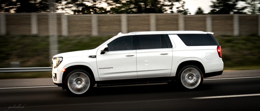 White GMC Yukon SUV driving quickly on a highway, motion blur in the background.