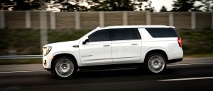 White GMC Yukon SUV driving quickly on a highway, motion blur in the background.