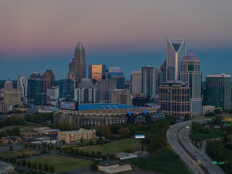Dusk over a Downtown Skyline with Tall Glass Towers a Large Stadium in the Foreground and a Curving Highway in Front